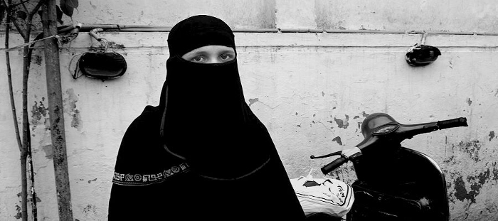 Black-and-white street photograph of a woman in a hjjab