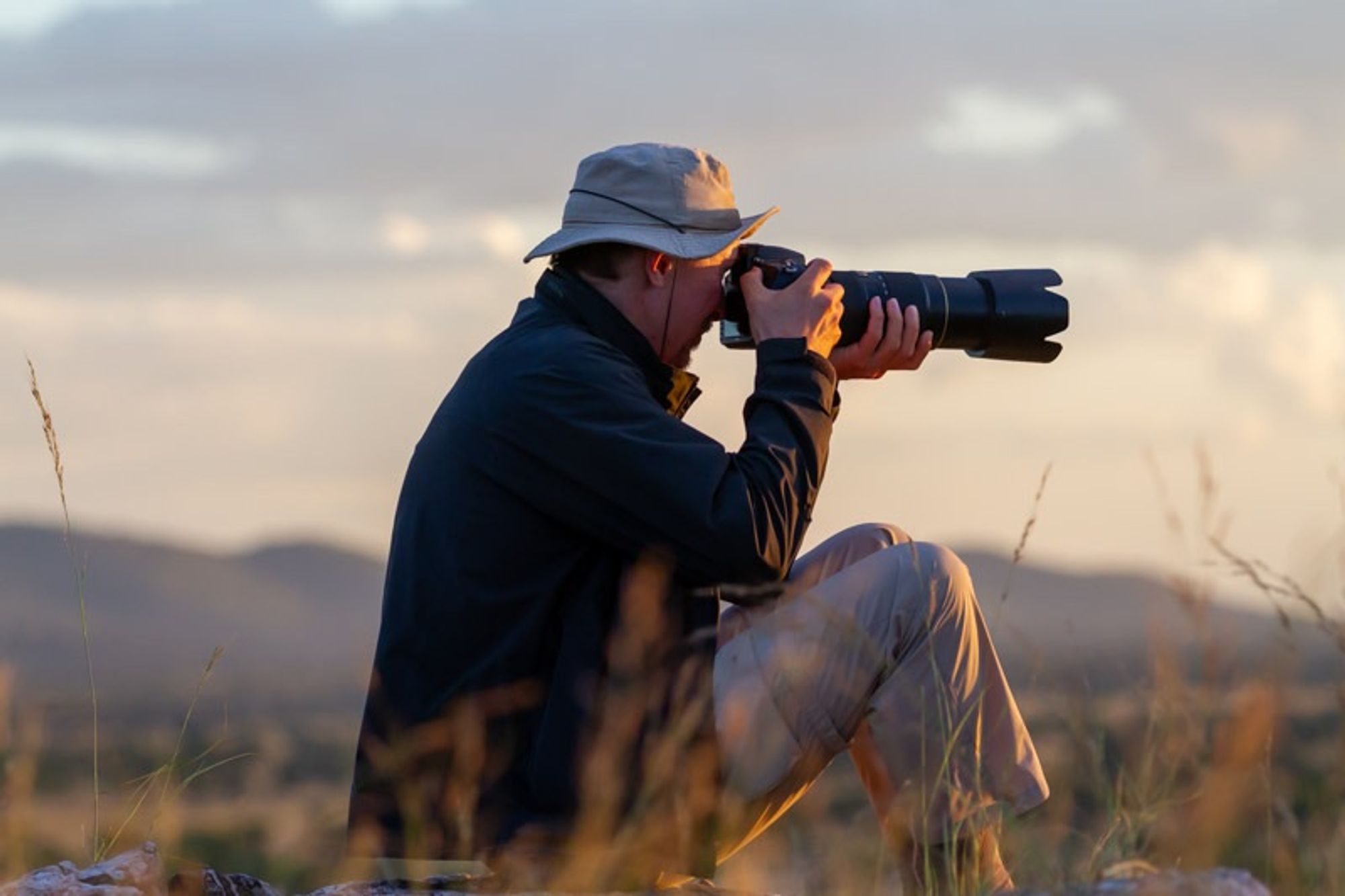 Photographer sitting and taking a picture outdoors with a a rugged camera