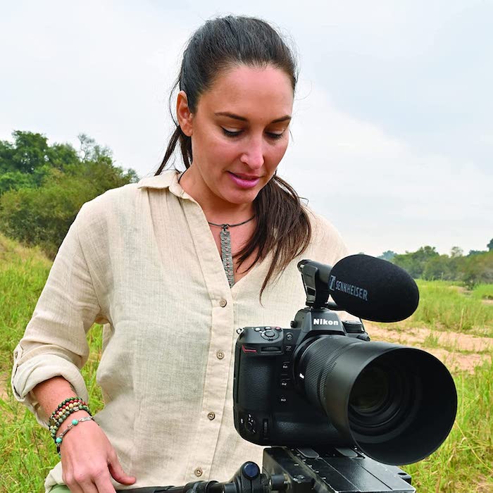 A woman standing in a field outside over the best Nikon mirrorless camera (Z9) with a lens and microphone attached