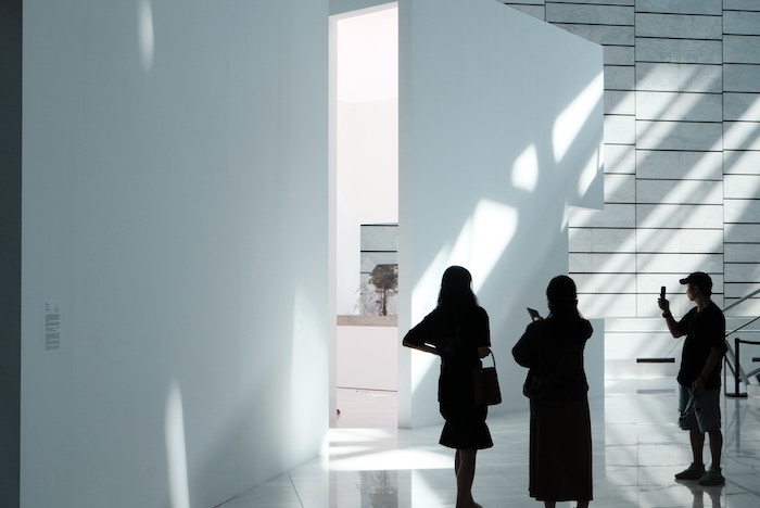 Silhouette of three people inside a white-walled room with low light