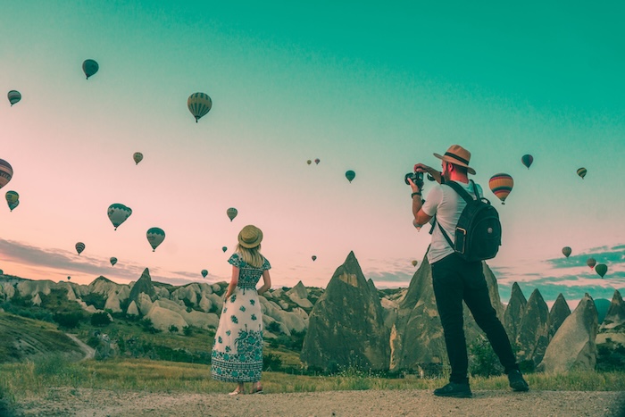 A woman posing for a travel photographer with a hot-air baloons in the background